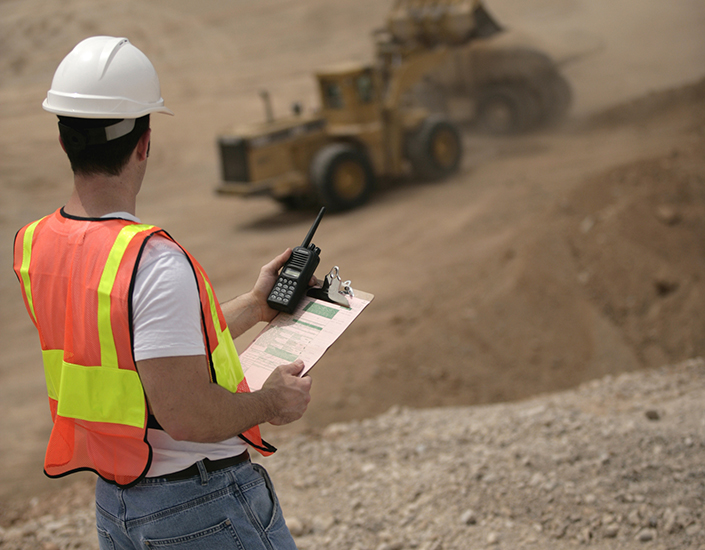 Construction worker overseeing bulldozer while holding a wireless radio